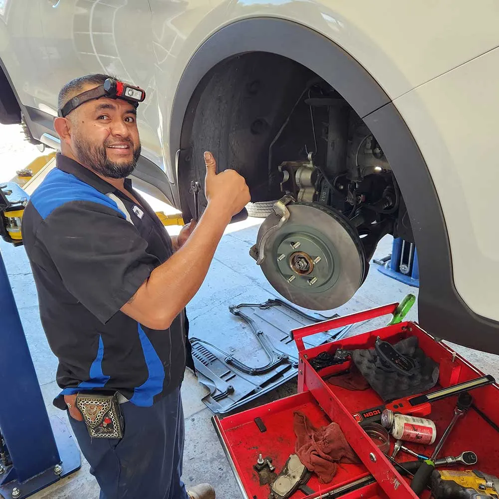 Mechanic giving thumbs up while repairing vehicle brakes.