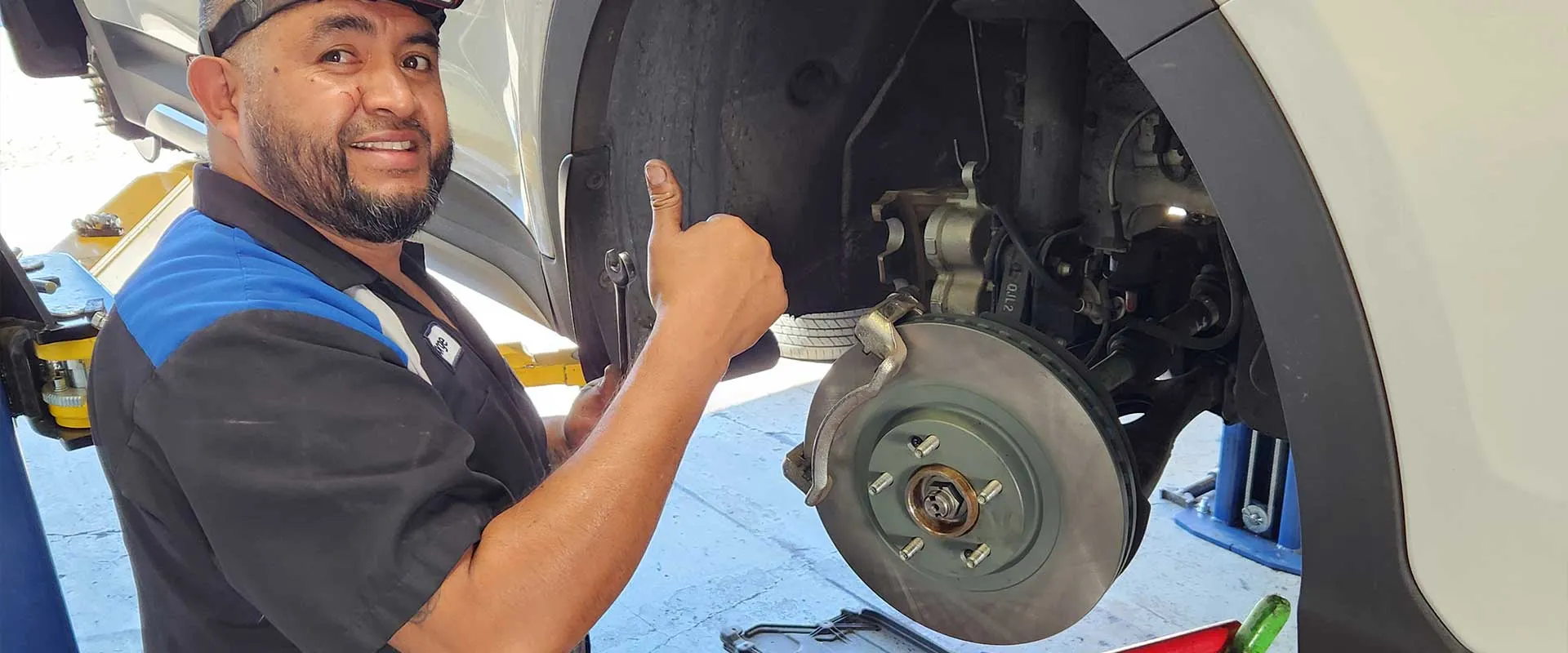Mechanic giving thumbs up near car brake repair.