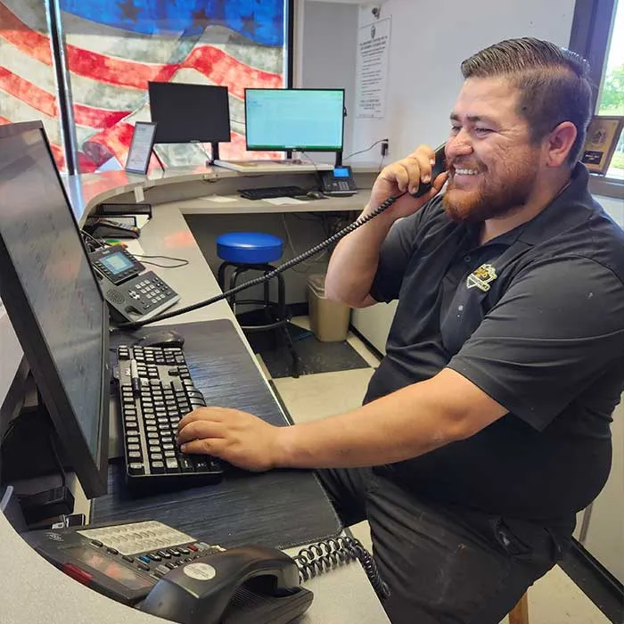 Smiling man at desk using phone and computer.